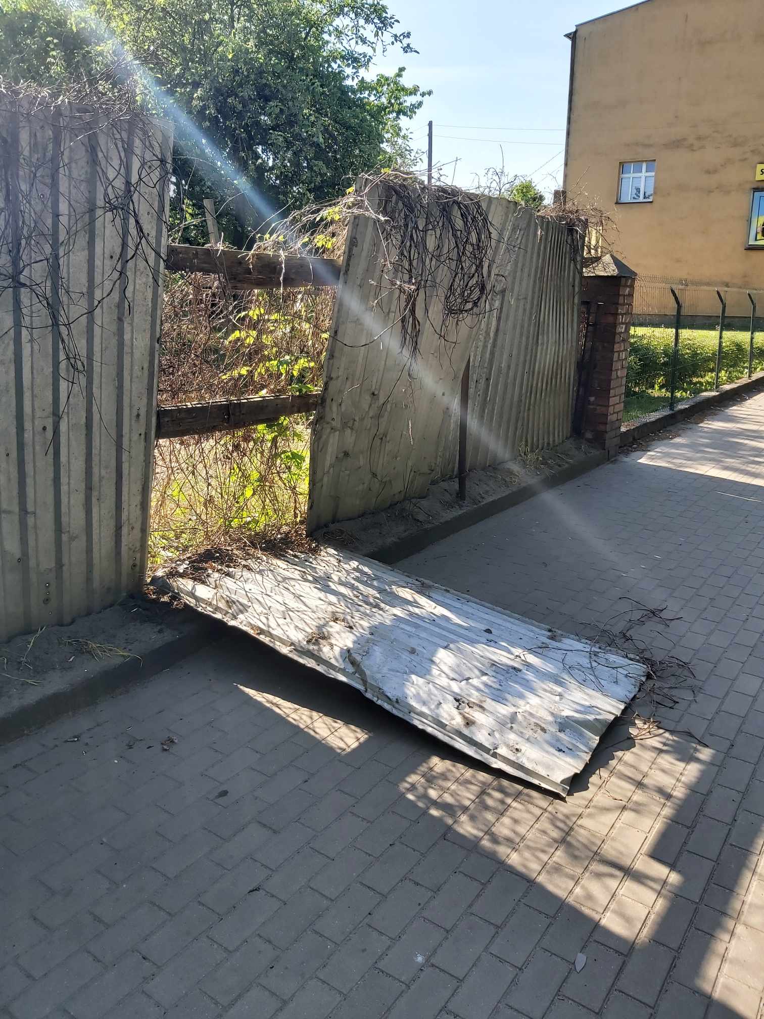 Na chodniku leży duży kawał blach w kształcie prostokąta, będący częścią płotu.