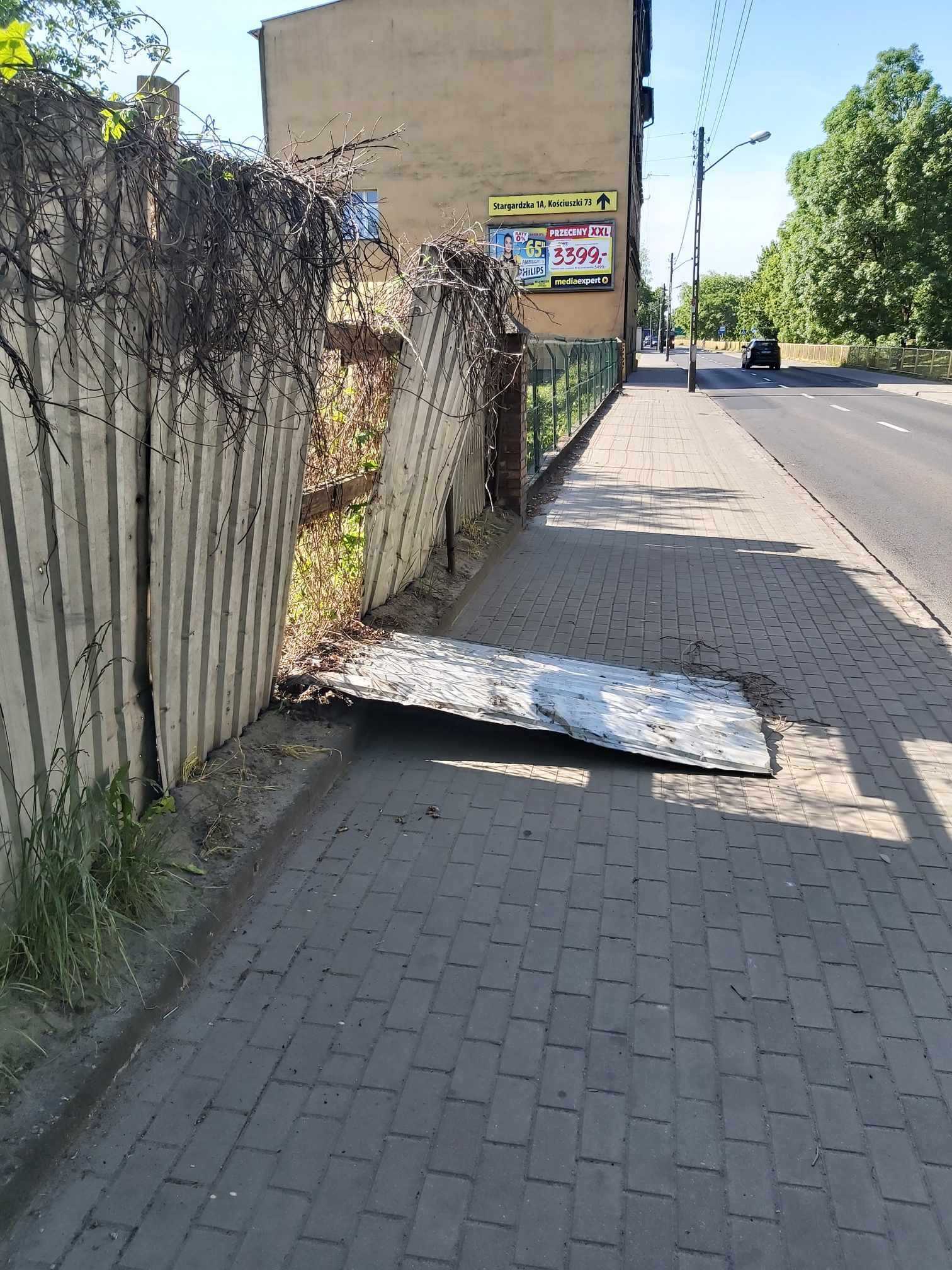 Na chodniku leży duży kawał blach w kształcie prostokąta, będący częścią płotu.