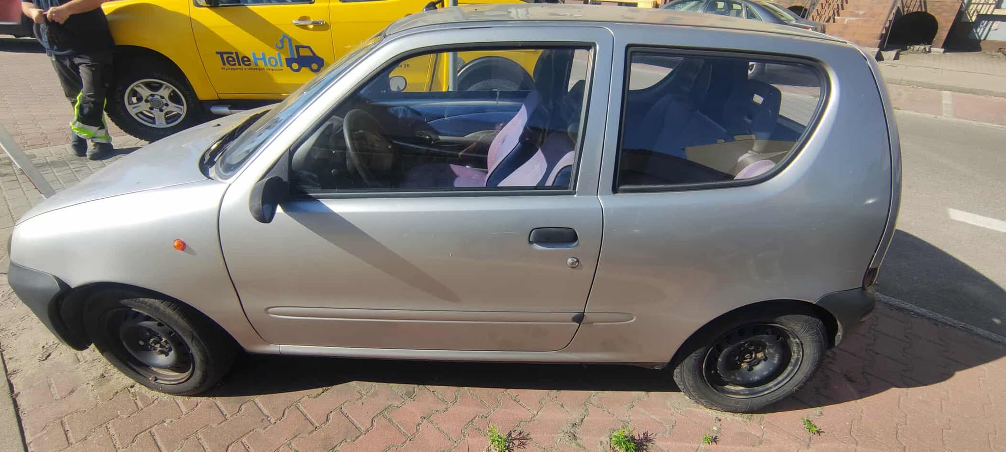 Na parkingu stoi stary i uszkodzony samochód marki fiat seicento.